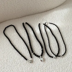 Black beaded necklace set with silver heart pendant on soft white faux fur background