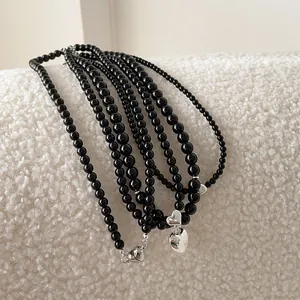 Layered black bead necklace with silver heart pendants on white textured background