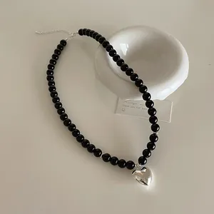 Detailed view of black beaded necklace featuring a polished silver heart pendant and lobster clasp