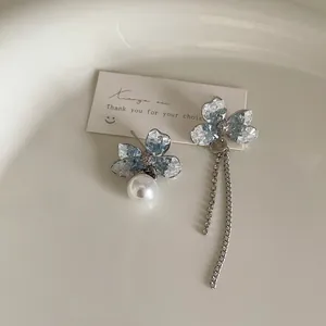 Detail of asymmetric floral earrings with blue crystal inlay, pearls, and long tassels