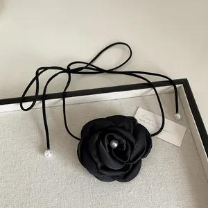 Detail of a black fabric rose choker with a white pearl center and thin satin ribbons