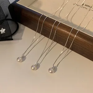 Détail de trois colliers en perles d'eau douce posés sur un plateau en bois brun