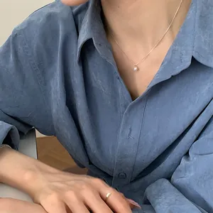 Détail d'un collier avec perle d'eau douce et bague fine dorée portés par un mannequin