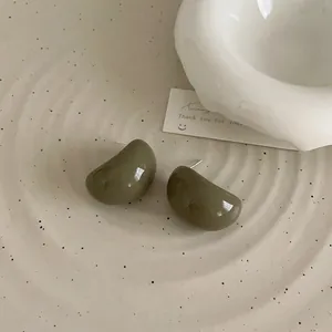 Gros plan de boucles d'oreilles en résine vert olive sur un plateau en céramique beige