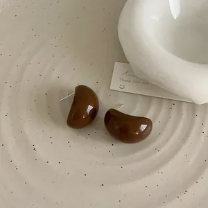 Détail de boucles d'oreilles en résine marron foncé poli sur un plateau en céramique design