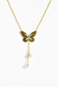 Detailed close-up of gold butterfly pendant with enamel wings and hanging pearl tassels