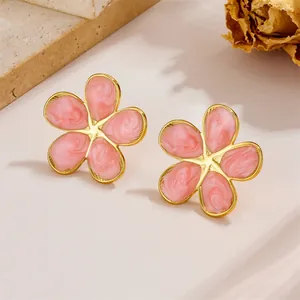 Elegant pink enamel floral stud earrings with gold plating on a stone display