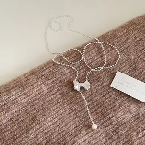Close-up of silver beaded necklace with bow pendant and white pearl on knit fabric
