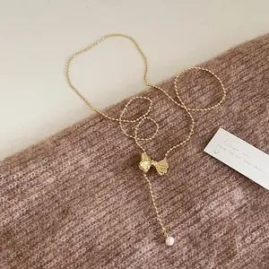 Detail of a vintage golden bead necklace with bow pendant and a dangling white pearl