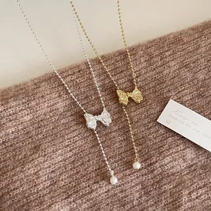 French vintage metal bow necklace with pearl pendant on brown knit sweater background
