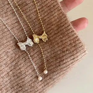 French vintage metal bow necklace with delicate bead chains and pearl drops on a brown knit background