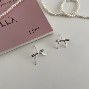 Detailed view of silver bow-shaped metal stud earrings on a minimalist decorative background