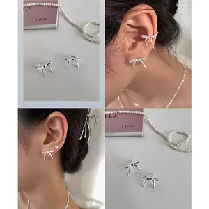 Detailed view of silver bow-shaped stud earrings and ear cuffs with a polished metallic finish