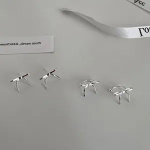 Detailed macro view of silver bow-shaped stud earrings and ear cuffs on gray surface