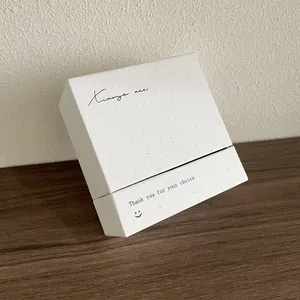 Détail d'un coffret cadeau bijoux minimaliste en papier texturé blanc sur bois sombre