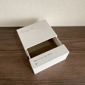 Détail d'une boîte à bijoux blanche avec message de remerciement sur surface en bois