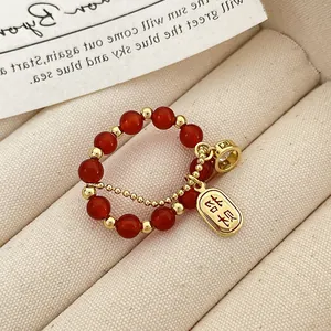 Detalle de anillo de cuentas rojas con amuleto Pingan dorado y colgante de circón