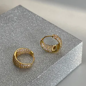 Macro shot of gold-plated hoop earrings with pavé white zircon stones on a silver stand