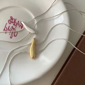 Detail of minimalist matte gold and silver teardrop necklaces on elegant ceramic plate