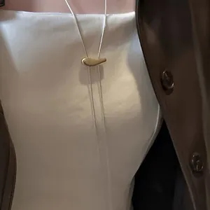 Detail of elegant gold bean pendant on long chain necklace for women styled with a coat