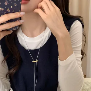 Detail of matte gold bar pendant with thin silver chain worn over a navy sweater
