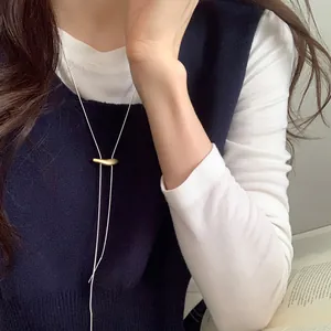 Detail of minimalist gold droplet pendant with silver cord on model's sweater