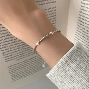 Detail of a minimalist silver star charm bracelet on a wrist with a soft knitted sleeve
