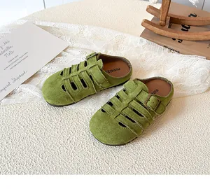 Detail of green suede hollow-out toddler clogs with vintage buckles on a lace background