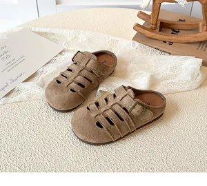 Detail of girls brown suede hollow out slippers with adjustable metal buckle on a woven mat