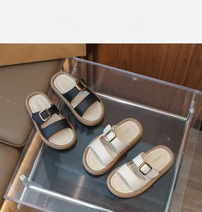Detailed view of girls' faux leather slides with large gold buckles in black and beige