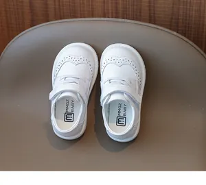 Detail of white girls' leather shoes featuring elegant brogue patterns and hook-and-loop strap