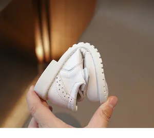 Close-up of flexible white leather girls shoes with non-slip sole and brogue details