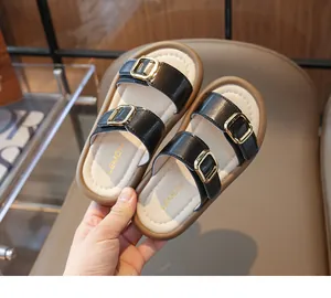Détail de sandales pour enfants avec brides en cuir noir et boucles métalliques dorées