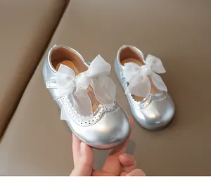 Detail of silver baby Mary Jane shoe with large white mesh bow and brogue cutouts