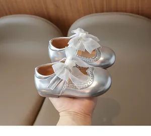 Close-up of silver girls' Mary Janes with large white organza bow and wavy cutouts