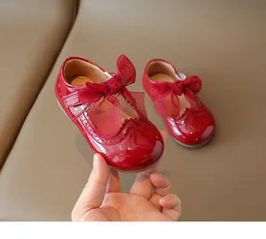 Close-up of red patent leather girl shoe featuring a large mesh bow and brogue detailing
