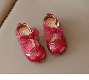 Detail of red patent leather Mary Jane shoes with brogue patterns and organza bows