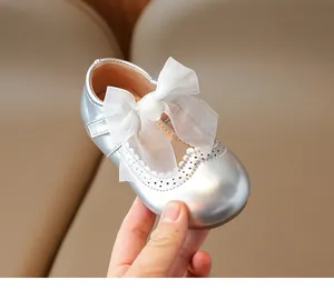 Close-up of silver girls' Mary Janes with white organza bow and brogue detailing