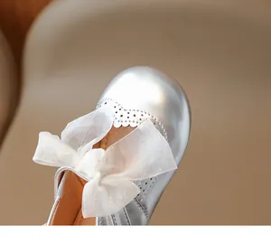 Detailed close-up of silver girls' shoes featuring a mesh bow and elegant brogue carvings