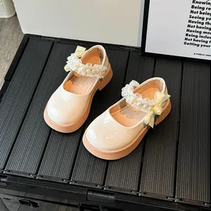 Glossy beige girls Mary Jane shoes with pink rubber soles and a yellow silk bow detail