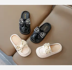 Detailed top view of kids' mule shoes with pearl bow and rhinestones in black and beige