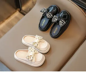 Detail of girls' loafers featuring pearl and rhinestone bow accents on black and beige leather