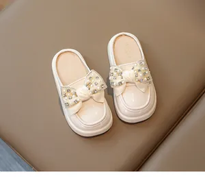 Close-up of pearl and rhinestone bow on cream patent leather girls' mule slippers