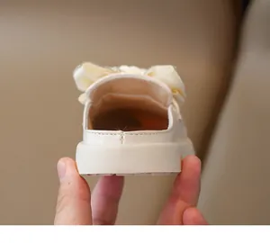 Detail of girls' cream mule shoes with glossy finish and large decorative bow ornament