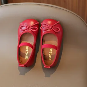 Classic red girls' Mary Jane shoes with bow detail and elastic strap on a leather background