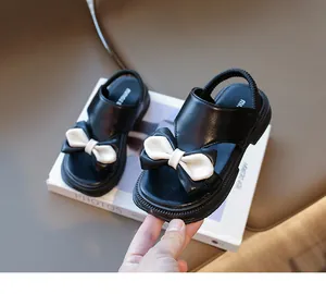 Nahaufnahme der schwarzen Mädchen-Sandalen mit Kontrastschleife und elastischem Fersenriemen