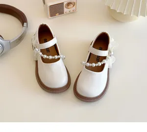 Detail of white girls Mary Jane shoes with pearl and lace bow on brown rubber sole