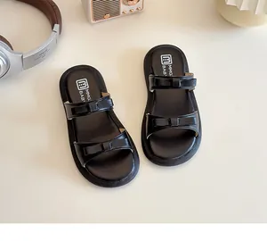 Detail shot of black kids slippers with double bow straps on a warm lifestyle background