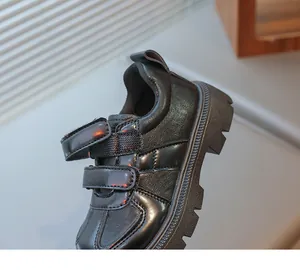 Detail of children's black leather shoes featuring dual velcro straps and anti-slip thick soles