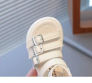 Close-up of off-white girls' Roman sandals featuring silver buckles and stitched footbed